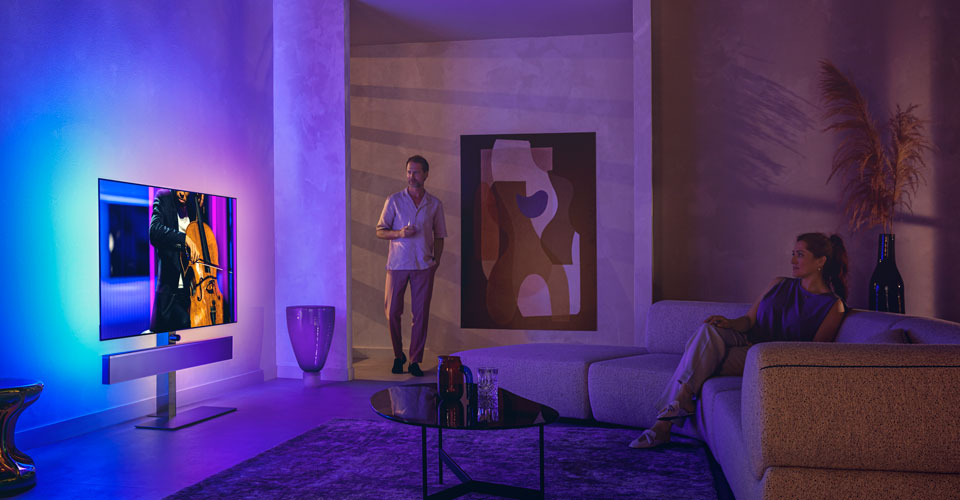 F&eacute;rfi &eacute;s nő egy st&iacute;lusos nappaliban, ahol egy csell&oacute;előad&aacute;st k&ouml;zvet&iacute;tő Philips Ambilight t&eacute;v&eacute;t n&eacute;znek