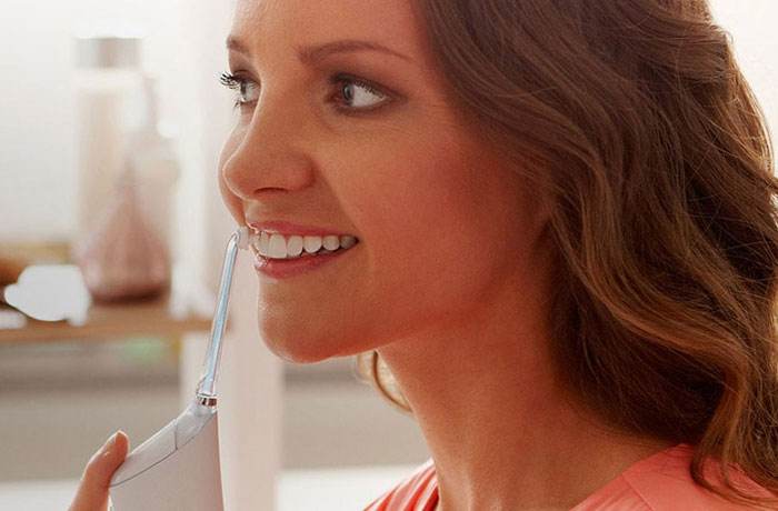 Egy nő hófehér fogait mossa egy Philips Sonicare Airfloss elektromos fogkefével.